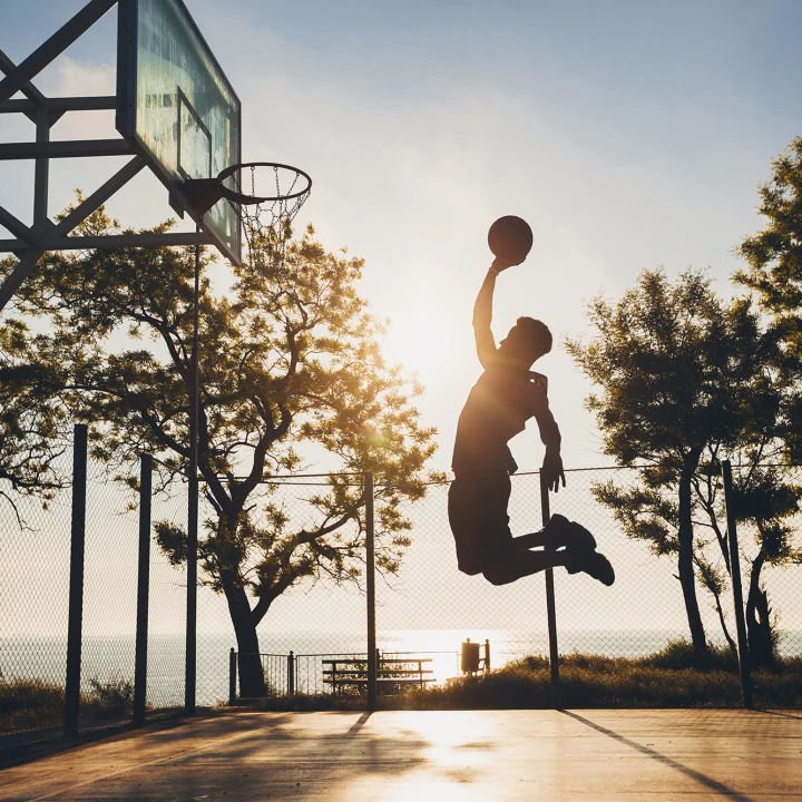 black man doing sports, playing basketball on sunrise, jumping silhouette