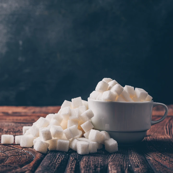Side view white sugar cubes in a cup on dark and wooden backgrou
